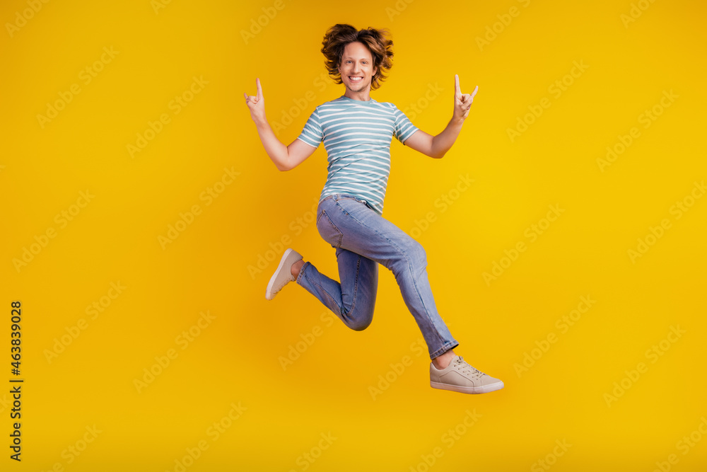 Full size photo of young cheerful man happy positive smile jump show fingers rock sign isolated on shine yellow background
