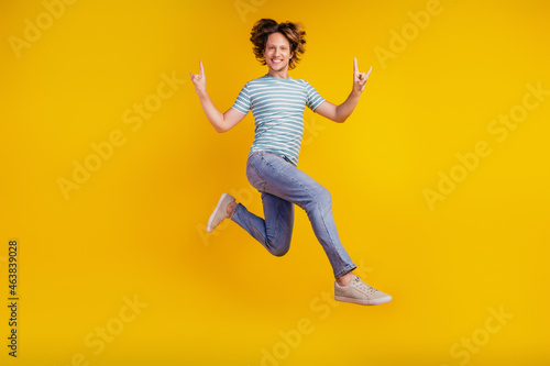 Full size photo of young cheerful man happy positive smile jump show fingers rock sign isolated on shine yellow background © Tetiana