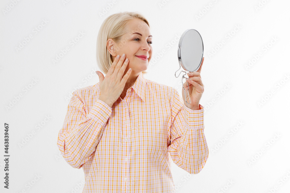Happy Middle aged Woman looking in mirror on her face with wrinkles on the forehead and wrinkle skin. Collagen and face injections concept. Menopause. Copy space and mock up. Happy Middle aged Woman looking in mirror on her face with wrinkles on the forehead and wrinkle skin. Collagen and face injections concept. Menopause. Copy space and mock up.