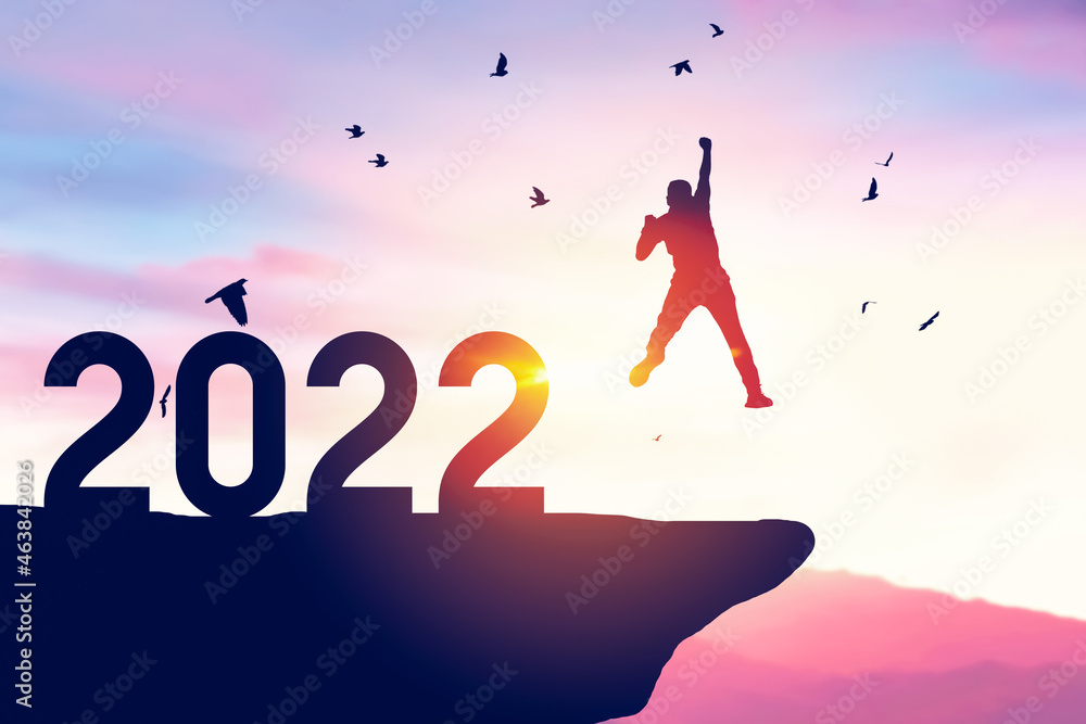 Man jumping on sunset sky with birds flying at top of mountain and number like 2022 abstract background. Man jumping on sunset sky with birds flying at top of mountain and number like 2022 abstract background.