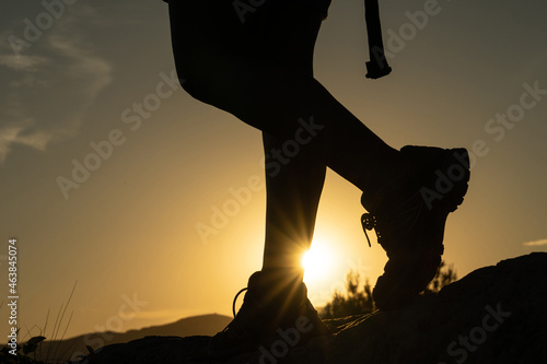 Silhouette of the legs of a woman doing trekking in the mountain with the sun creating a sunstar with her foot at sunset