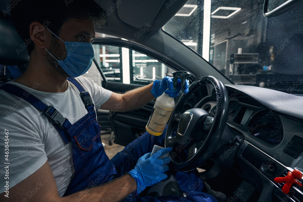 Worker washing car steering wheel with cleaning spray