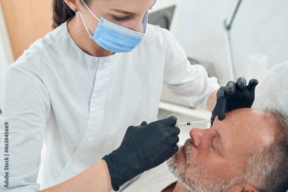 Cosmetologist in medical mask making injection in man face Cosmetologist in medical mask making injection in man face