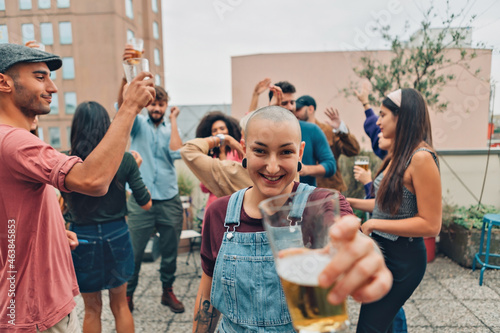 smiling hipster girl at the party - cheerful young woman cheering - young alternative lady stretches her arm offering a sip of beer to friends © Carlo