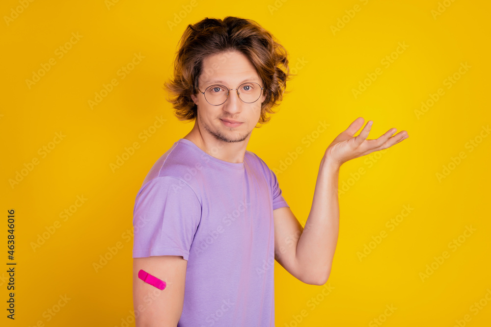 Uncertain funny clueless vaccinated man show plaster hand on yellow background Uncertain funny clueless vaccinated man show plaster hand on yellow background