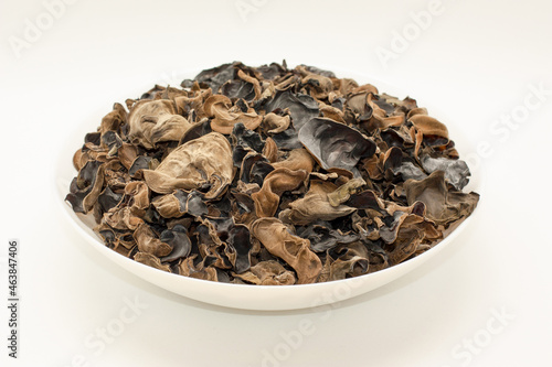 Dried Auricularia mushrooms lie in a round plate, on a white table.