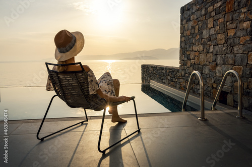 relaxing vacation - woman sitting in chair on terrace in front of pool and enjoying sunrise at luxury villa © ronstik