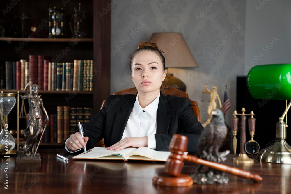 Young female lawyer during work in chamber. Gavel and Themis statue on the brown shining desk. Young female lawyer during work in chamber. Gavel and Themis statue on the brown shining desk.