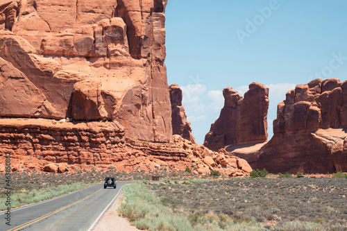 A car drives on the road toward red sandstone cliffs and rock towers in Arches National Park, Utah, USA.