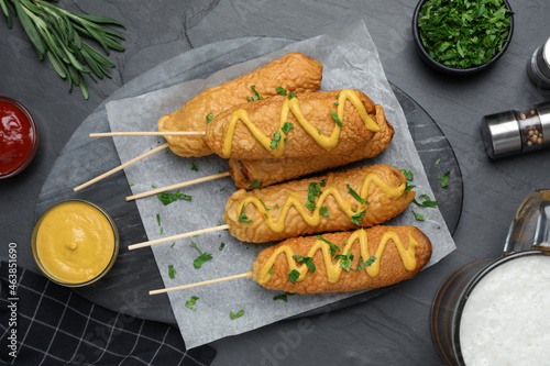 Photography Delicious deep fried corn dogs and sauces on black table, flat lay