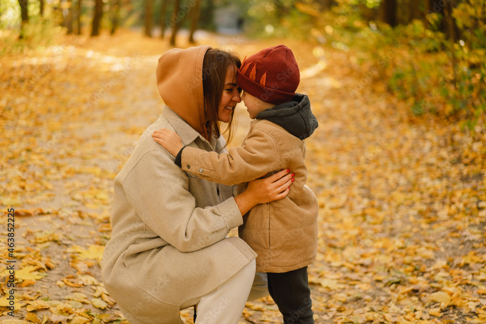 Fototapeta premium Happy young mother and son are walking in the autumn forest. Autumn outdoor activity for family with kids. Happy mother's day. Family day. Autumn day. Happy family leisure.