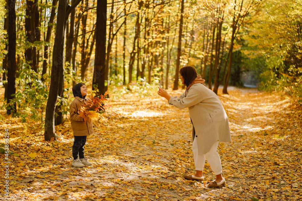 Fototapeta premium Mom and son take a selfie on the phone in the autumn forest. People use technology. Autumn outdoor activity for family with kids. Happy mother's day. Family day. Autumn day. Happy family leisure.