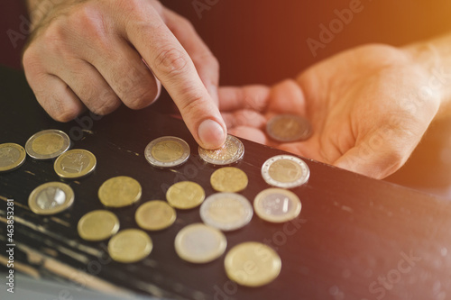 business man counting money. rich male hands holds and count coins of different euros on table in front of a laptop. flare