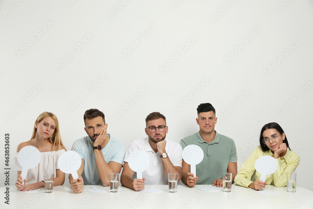 Panel of disappointed judges holding blank score signs at table on white background. Space for text Panel of disappointed judges holding blank score signs at table on white background. Space for text