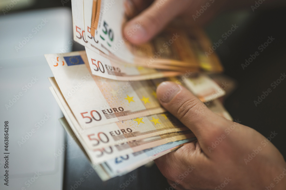 business man counting money. rich male hands holds and count cash banknotes of 50 euros bills or notes currency in front of a laptop business man counting money. rich male hands holds and count cash banknotes of 50 euros bills or notes currency in front of a laptop