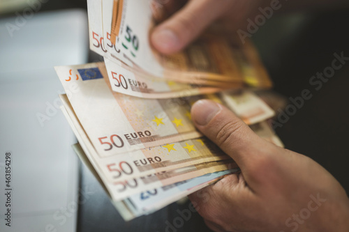 business man counting money. rich male hands holds and count cash banknotes of 50 euros bills or notes currency in front of a laptop