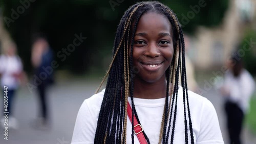 Close-up of pretty dark-skinned young woman student with afro-braids smiling while posing for portait in university park. Portrait of cheerful african american college girl posing on camera outdoors