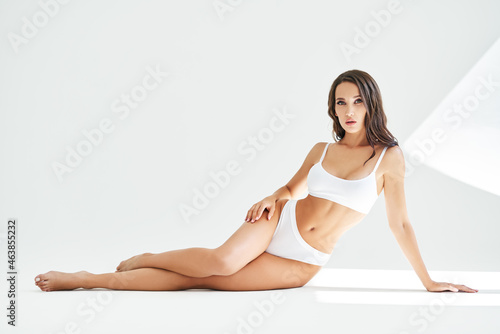 Young beautiful woman with perfect body in underwear sitting on floor posing on studio