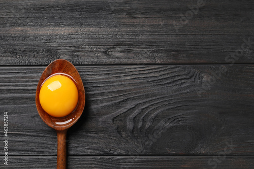 Obraz na płótnie Spoon with raw egg yolk on black wooden table, top view
