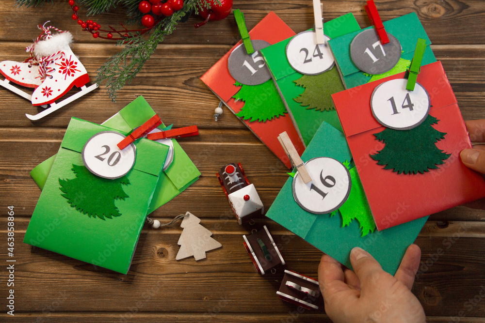 Fototapeta premium Christmas Advent calendar on the table, in a wooden box. Multicolored envelopes made by hand