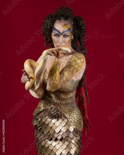 Portrait of a girl in golden scales with a yellow snake in her arms