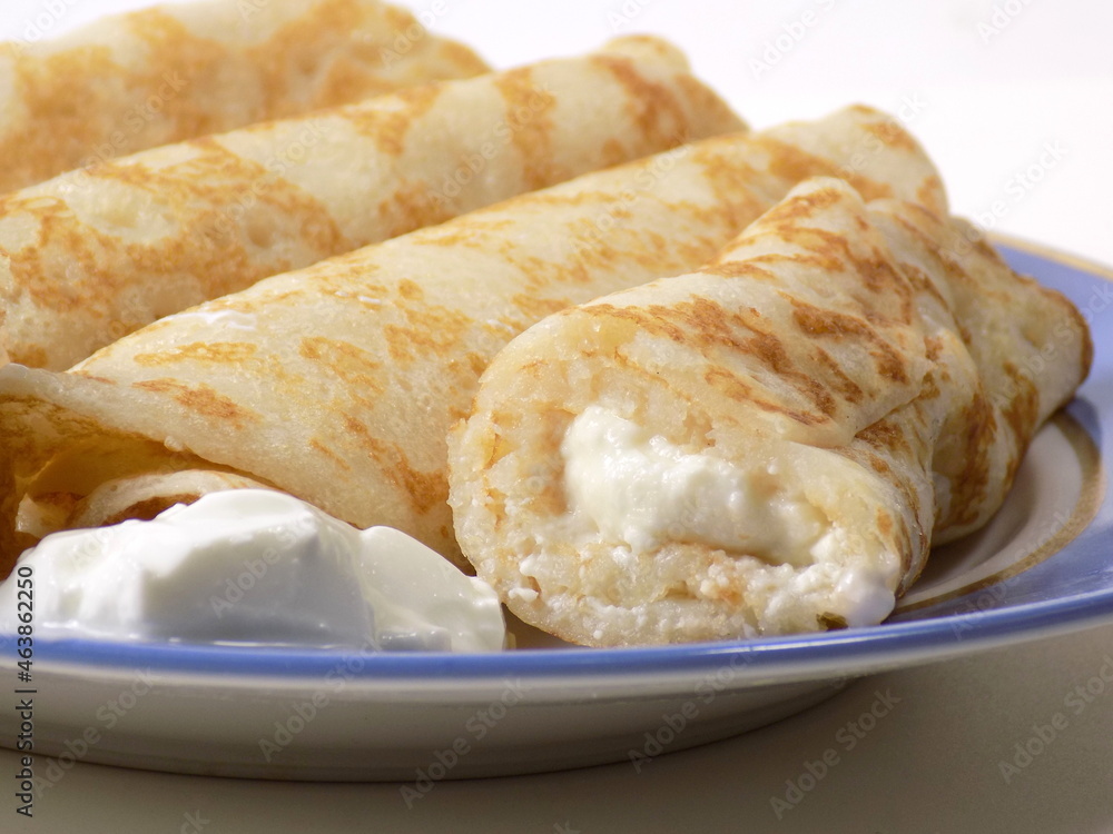 Pancakes stuffed with cottage cheese and sour cream on a plate. Close-up.