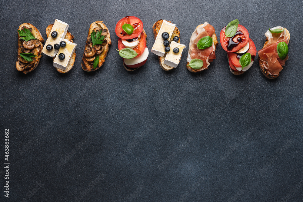 Bruschetta set with prosciutto and basil, tomatoes and mozzarella, camembert and berries, mushrooms and parsley on black background. Antipasto open sandwich appetizer