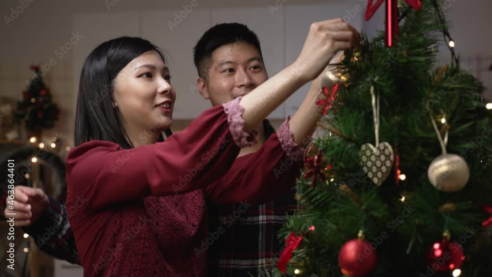 cheerful asian young couple in love decorating Christmas tree together to get ready for the winter holiday in the apartment cheerful asian young couple in love decorating Christmas tree together to get ready for the winter holiday in the apartment