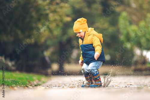 Photo Happy little kid boy jumping on rainy puddle in autumn on nature