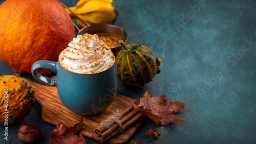 Pumpkin spice latte in a blue mug with whipped cream, cinnamon. Blue background decorated autumn leaves, pumkin.