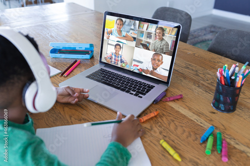 African american boy using laptop for video call, with diverse elementary school pupils on screen photo