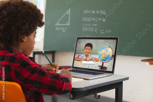 African american boy using laptop for video call, with biracial elementary school pupil on screen photo