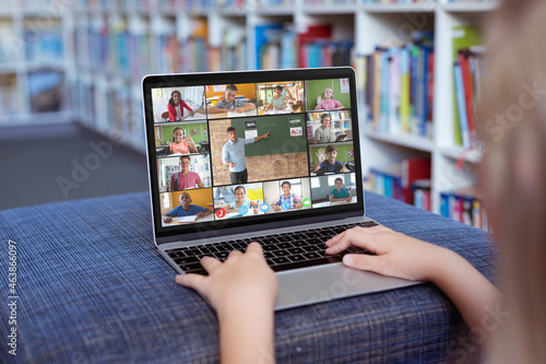 Caucasian girl using laptop for video call, with smiling diverse elementary school pupils on screen