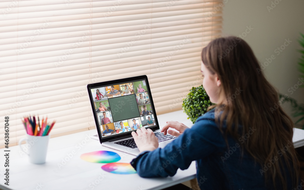 Caucasian girl using laptop for video call, with smiling diverse elementary school pupils on screen