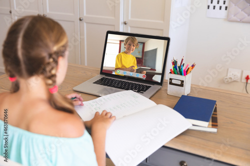 Caucasian girl using laptop for video call, with smiling elementary school pupil on screen