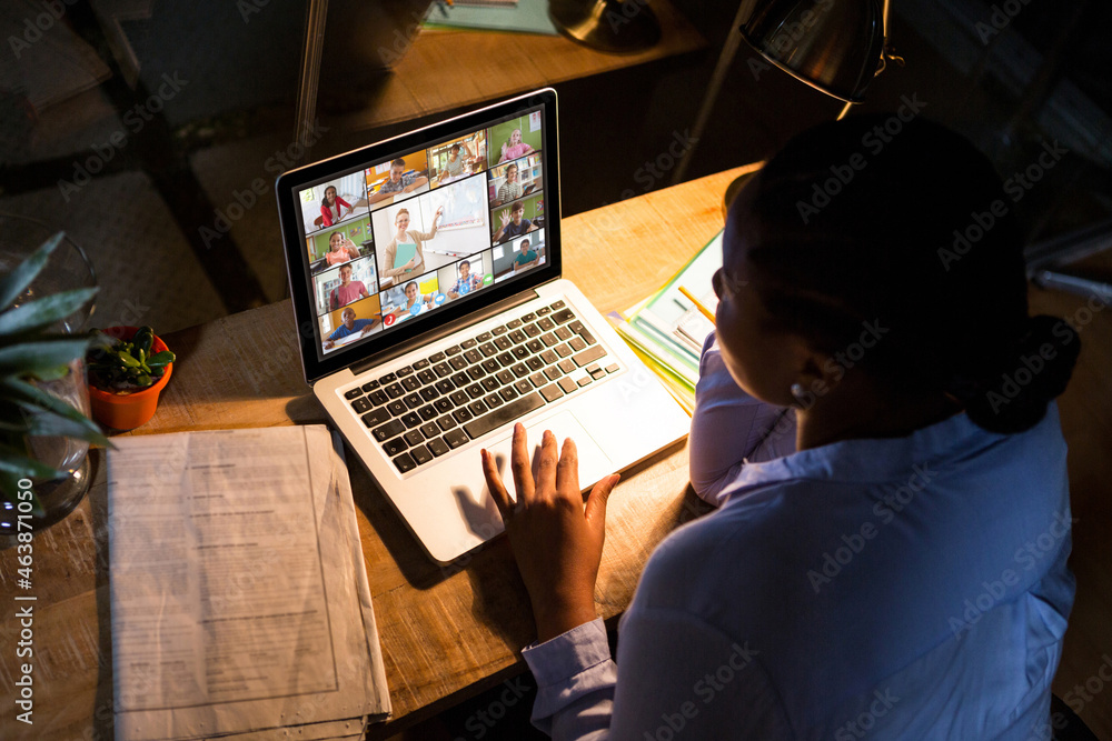 African american woman using laptop for video call, with diverse elementary school pupils on screen African american woman using laptop for video call, with diverse elementary school pupils on screen