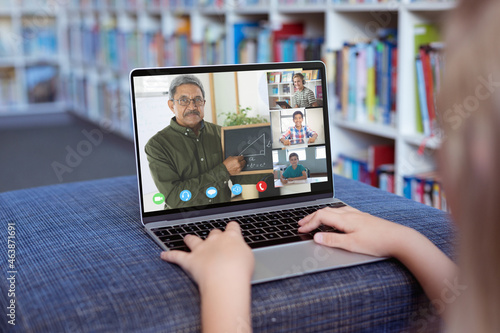 Caucasian girl using laptop for video call, with smiling diverse elementary school pupils on screen