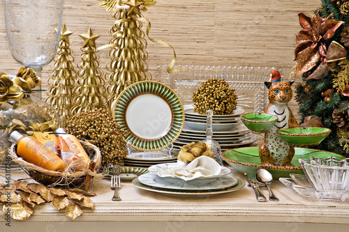 Mesa para o natal com uma decoração dourada com pequenas árvores de natal, pratos uma onça de porcelana. photo