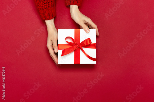 Fototapeta Naklejka Na Ścianę i Meble -  Christmas giving concept, top-down view of hands holding a gift box decorated with a red bow