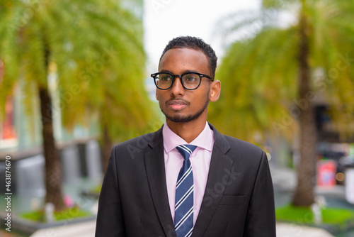 Portrait of handsome young African businessman thinking outdoors in city