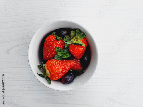  grapes and strawberries in white bowl on light wood background photo captured from above 