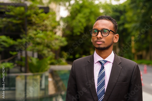 Portrait of handsome young African businessman thinking outdoors in city