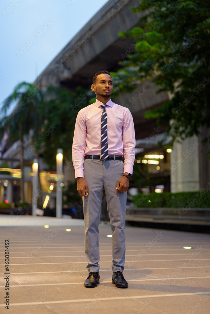 Full length portrait of handsome young African businessman outdoors in city at night thinking