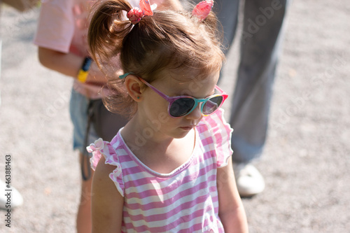Little sad beautiful girl in sunglasses and a striped dress on a walk