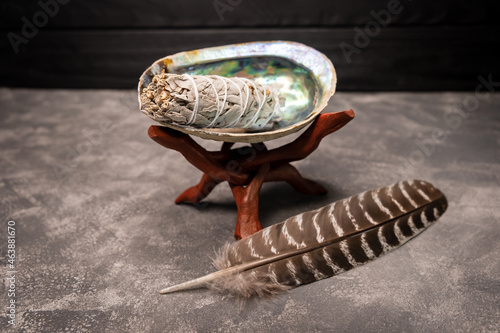 A close up image of a white sage bundle in an abalone shell. Smudge kit for spiritual practices with natural elements: dried white sage, sea pearl shell Abalone on grey background. Balancing the soul
