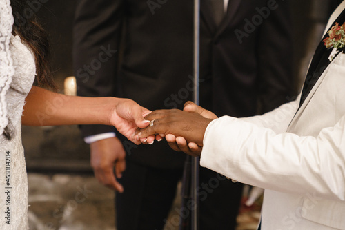 Fiance put the ring on the bride s hand Close up of hands of the bride putting a wedding ring on african american groom Loving couple of cute bride and african American groom