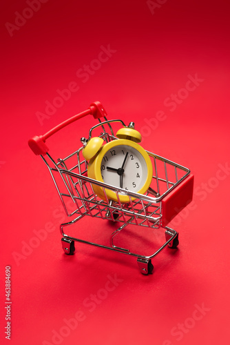 Shopping time. Yellow alarm clock in shopping basket on a red background. photo