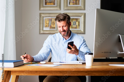 Middle aged businessman sitting at desk and using mobile phone while working from home © gzorgz