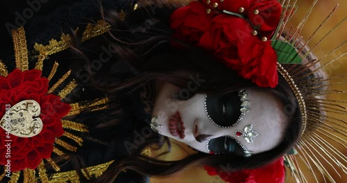 Vertical portrait of young woman with sugar skull makeup and red roses dressed in black costume of death as Santa Muerte. Day of the Dead or Halloween concept.