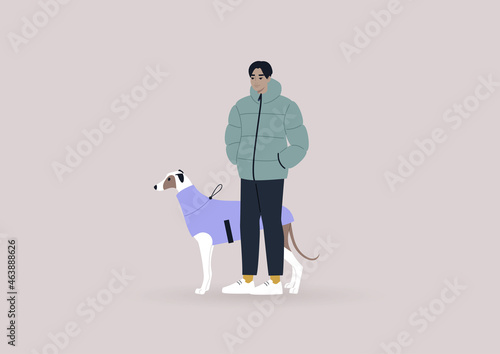 A young male Asian greyhound owner walking with their pet, winter season, dog clothes